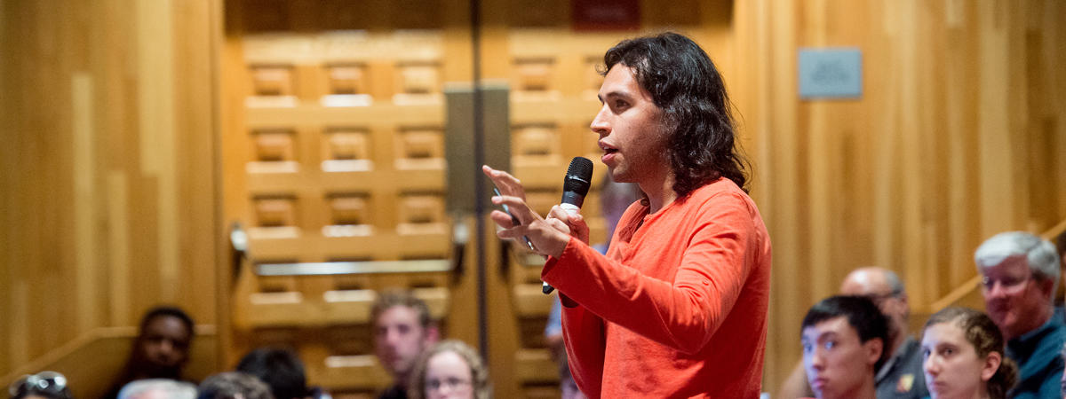 photo of all eyes on an audience member standing up to ask a poignant question during a lecture