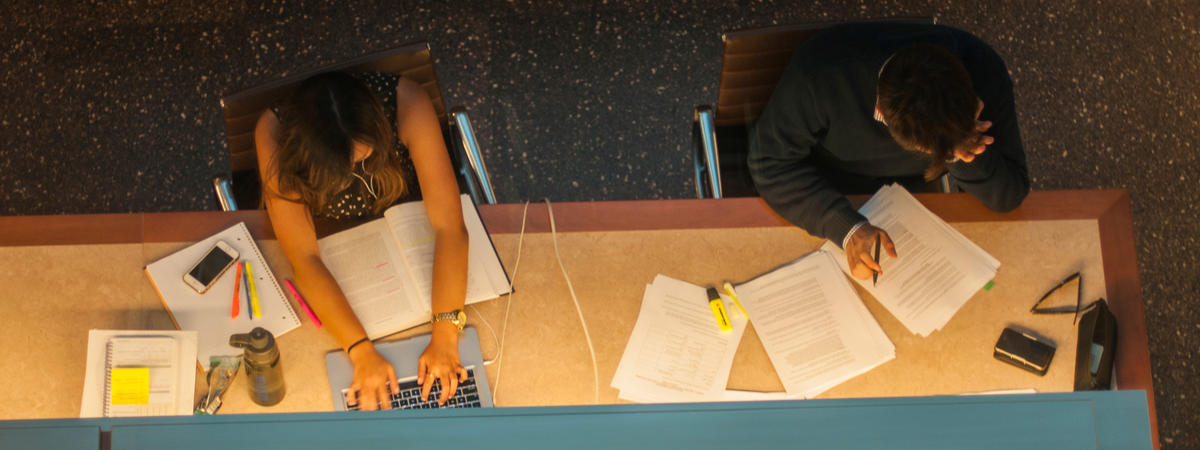 photo of 2 Boalt Hall students concentrating and frantically studying in library; materials and equipment scattered throughout
